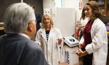 two people in lab coats explain something to a visitor in a suit