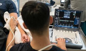 looking over a person's shoulder as they hold a sensor to a subject's arm and look at a readout on screen